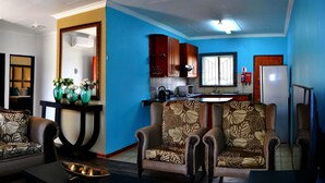 A living room with a sofa and armchairs, a dining table, and a kitchen area with cabinets and a refrigerator. - Lapologa Bed and Breakfast (Tzaneen)