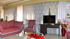 A living room with striped sofas, a flat-screen TV, a fireplace, and a dining table. - Lapologa Bed and Breakfast (Tzaneen)