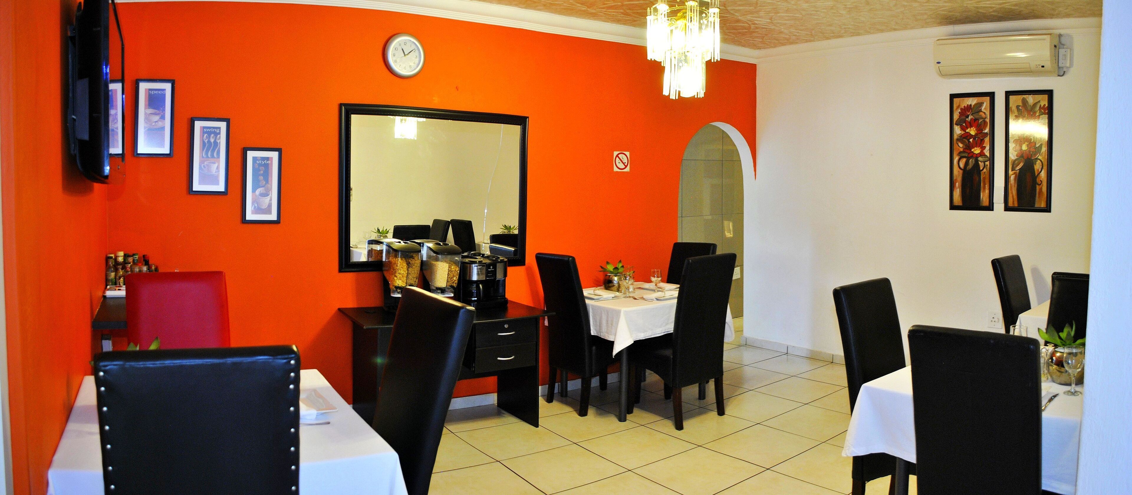 A restaurant with orange walls, black chairs, and a white tablecloth.