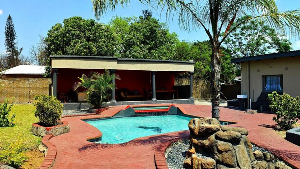 A pool area with a stone border, a small garden, and a building with a red facade. - Lapologa Bed and Breakfast (Tzaneen)