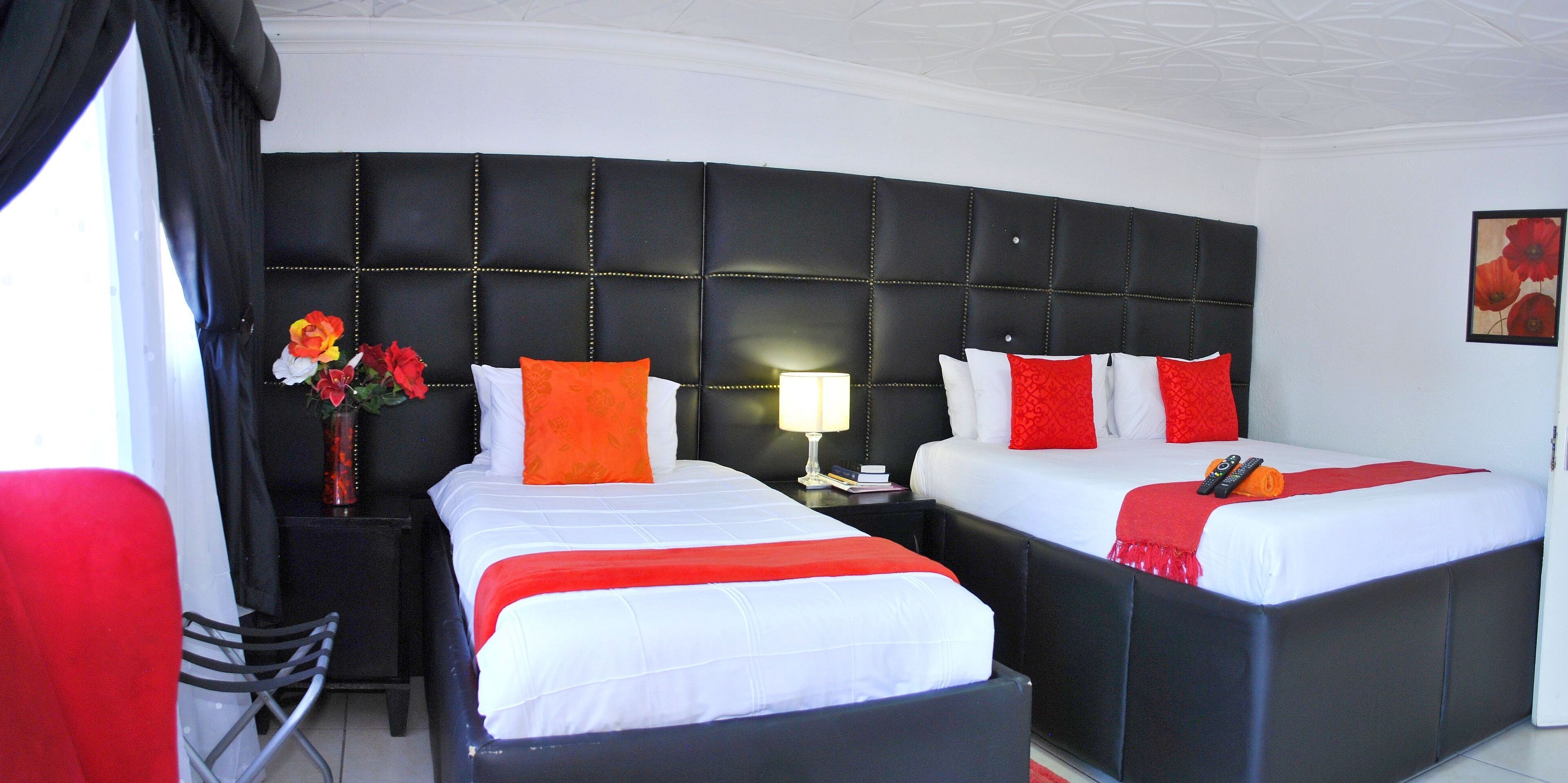 Habitación de hotel con dos camas, una mesita de noche con lámpara, un florero con flores y una silla roja.
