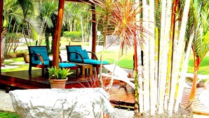 A covered outdoor seating area with wooden deck, two blue cushioned chairs, and a potted plant. - Flying Crocodile (Sámara)