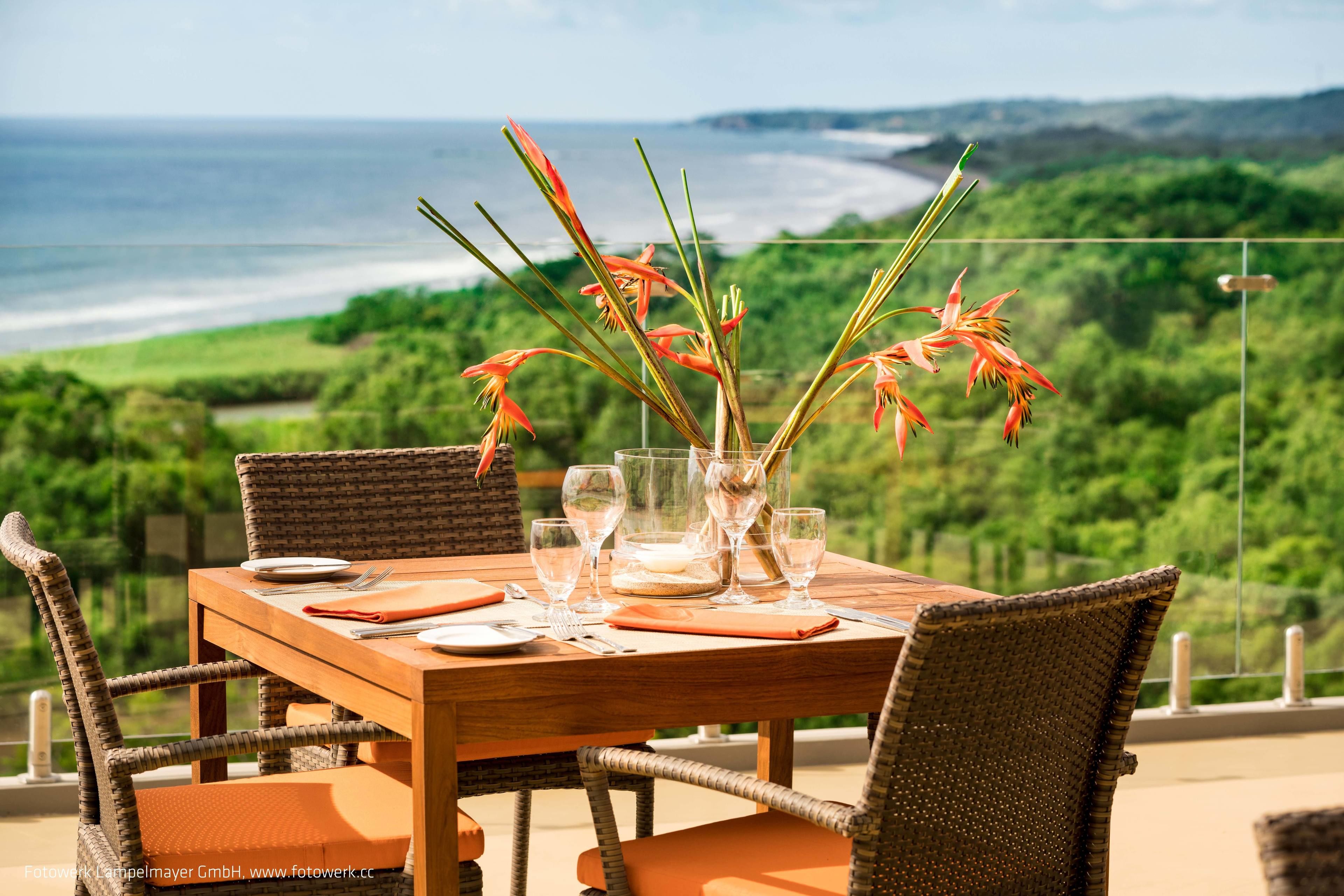 A wooden dining table with chairs, a vase with flowers, and empty wine glasses.