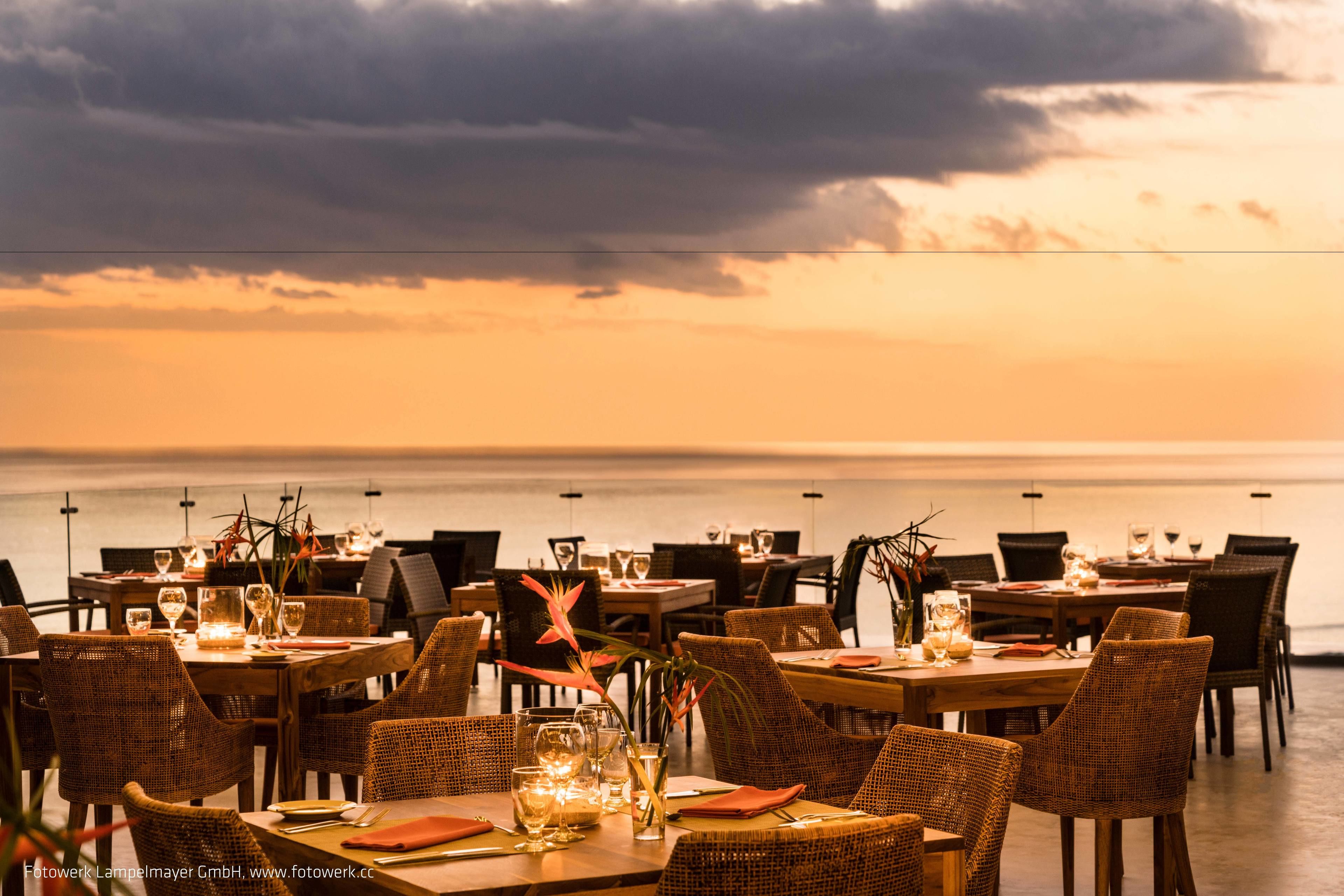 A restaurant with tables set for dining, overlooking the sea.