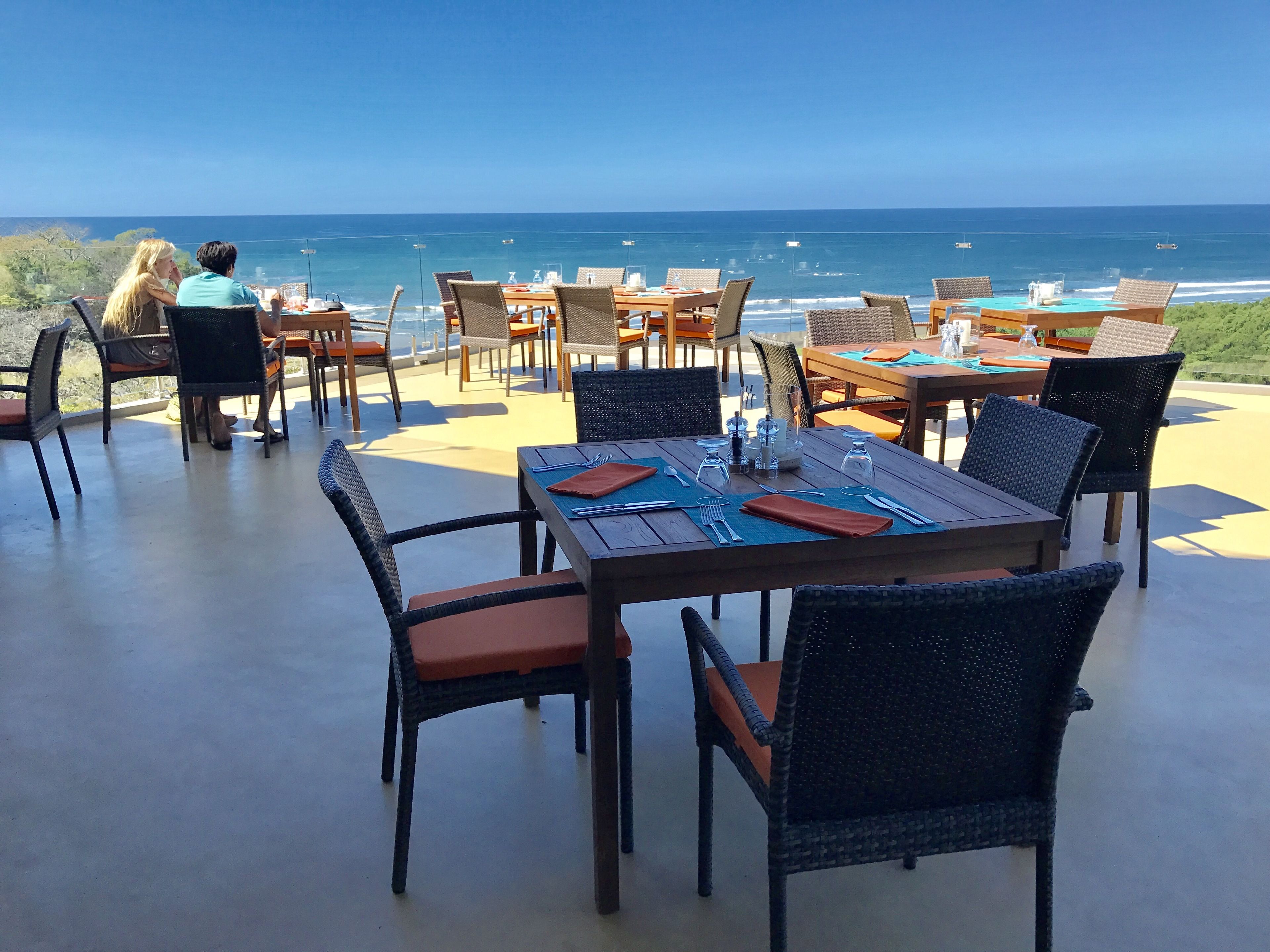 An outdoor dining area with tables and chairs, overlooking the ocean.