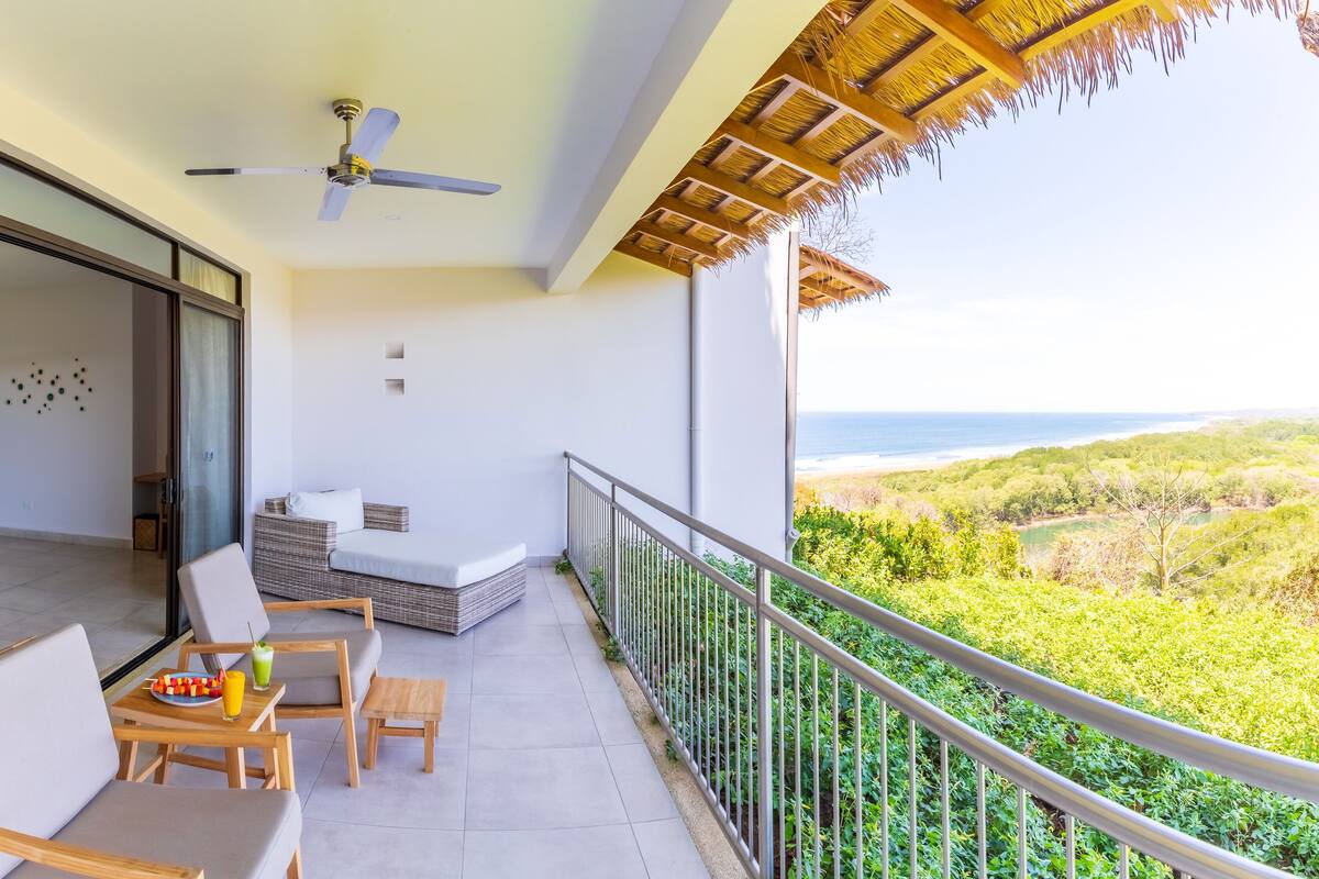 Un balcon avec vue sur l’océan, un ventilateur de plafond et un coin salon avec une table et des chaises.