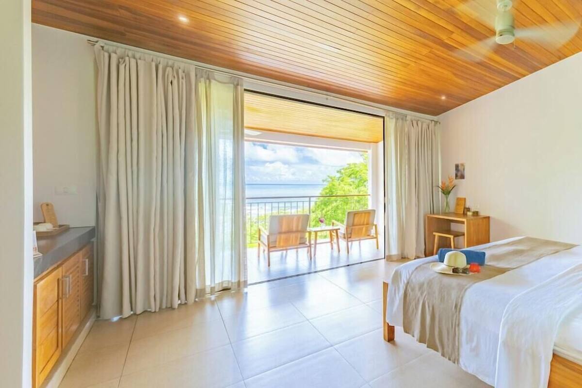 Une chambre à coucher avec un lit, un bureau et une chaise, un balcon avec des rideaux et une vue sur l’extérieur.