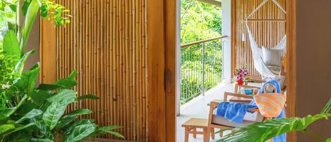 A wooden door leading to a balcony with a hammock, a table with a chair, and potted plants.