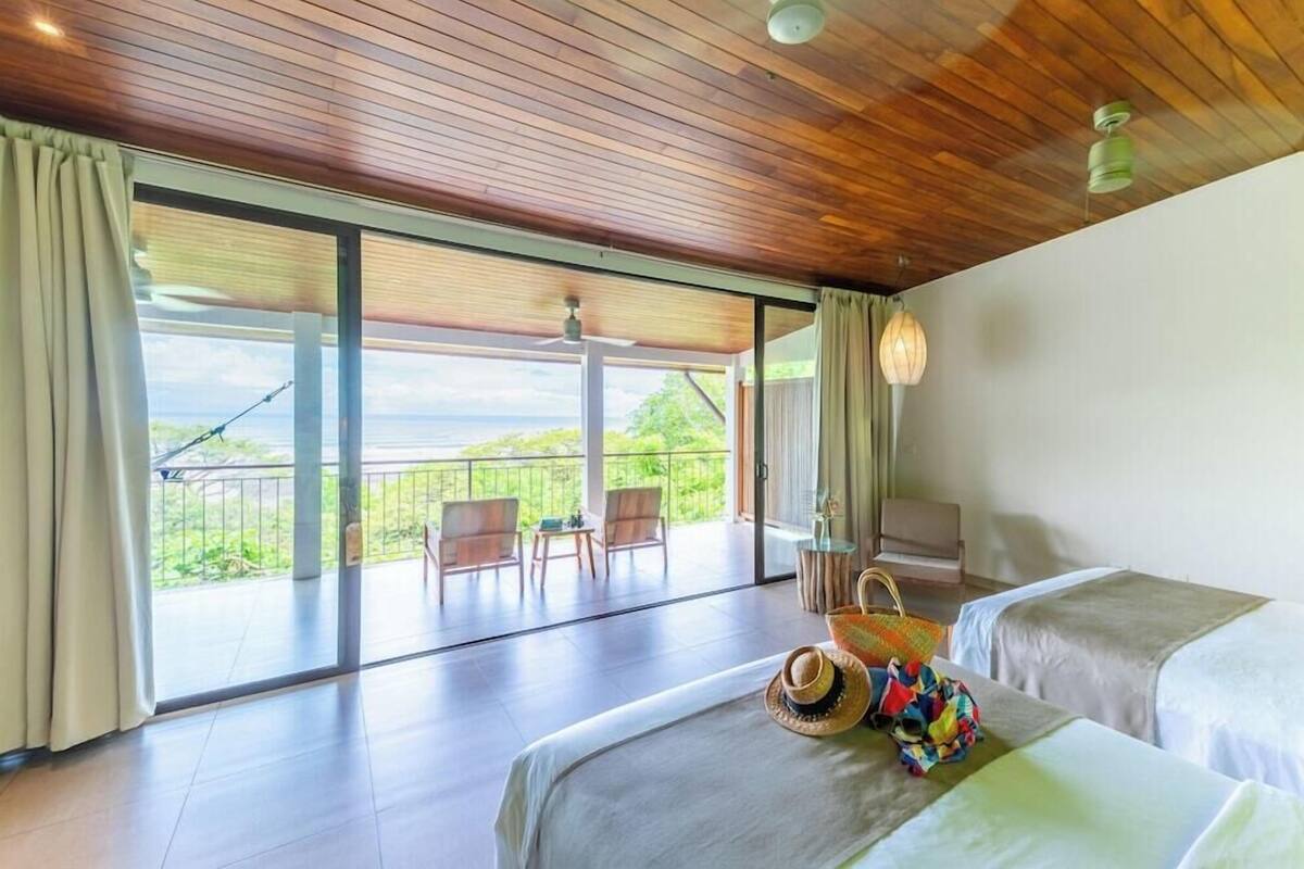 Une chambre d’hôtel avec deux lits, un balcon avec des chaises et une vue sur la verdure.