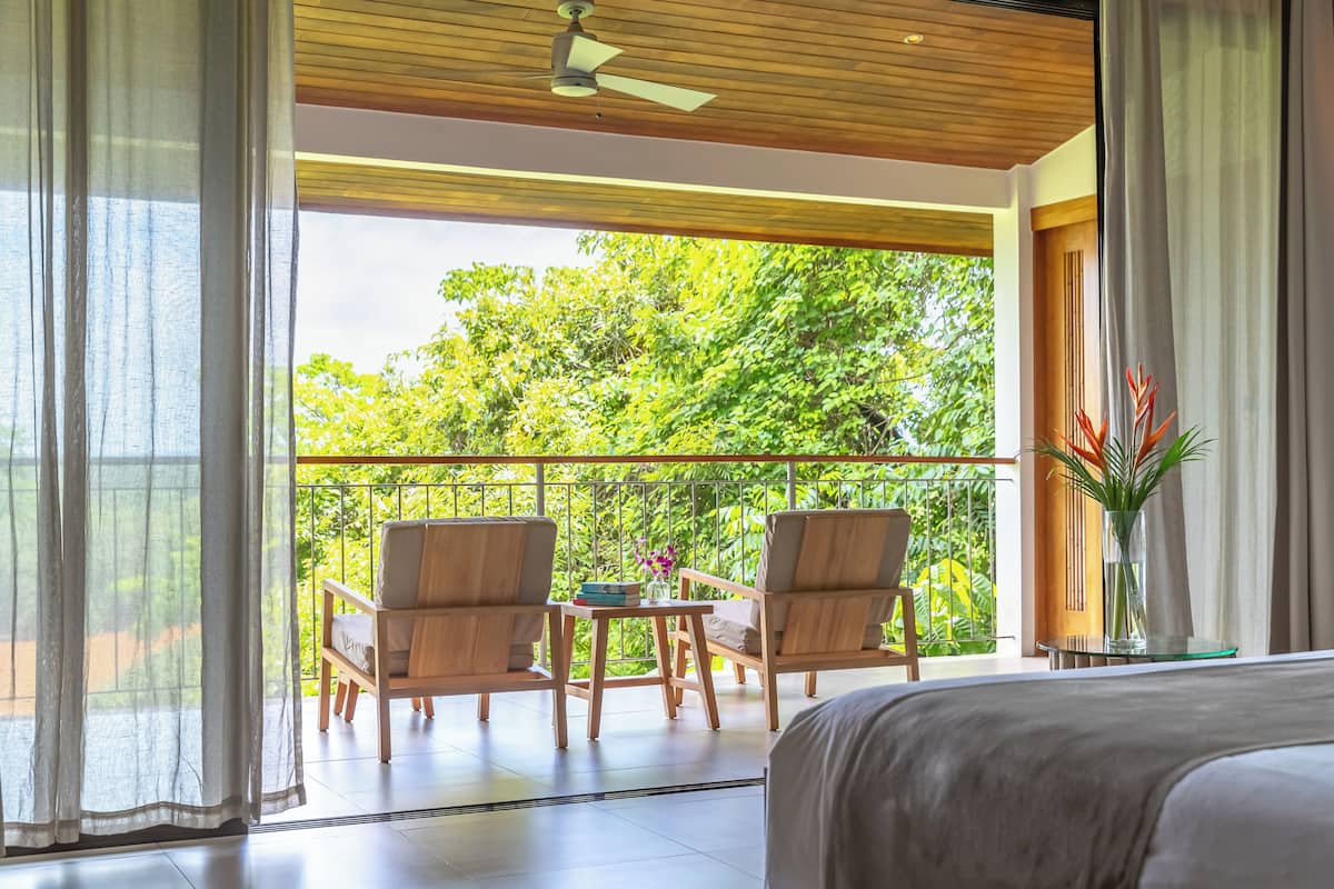 Un balcon avec des chaises et une table en bois, donnant sur une végétation luxuriante.
