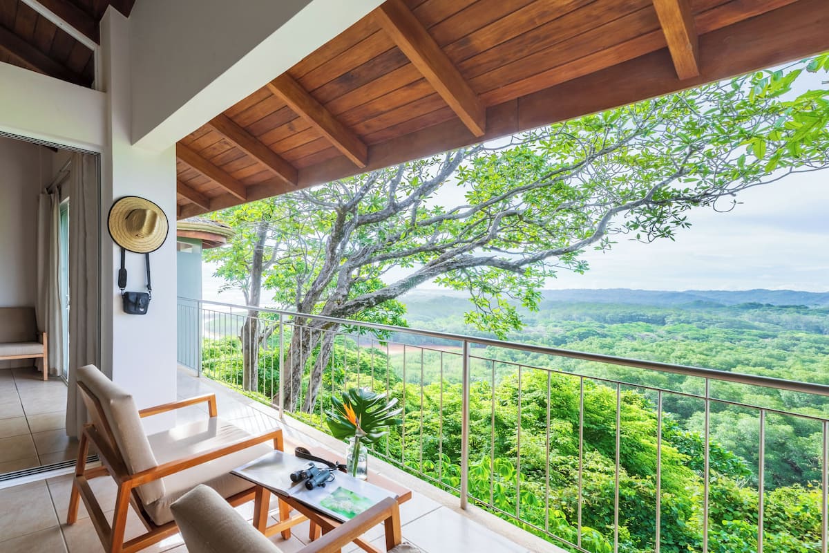 Un balcon doté d’un plafond en bois, d’une chaise, d’une table et offrant une vue sur un paysage verdoyant et luxuriant.