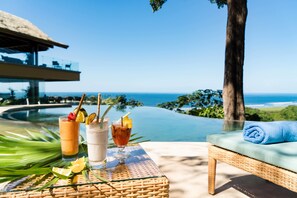 Un ambiente junto a la piscina con una silla de descanso, una mesa con bebidas y vistas al océano.