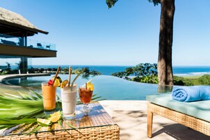 A poolside setting with a lounge chair, a table with drinks, and a view of the ocean.