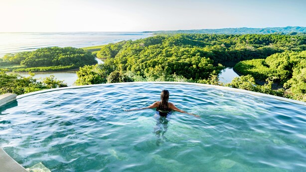 Una persona en un jacuzzi con vistas a un paisaje exuberante, con río y bosque.