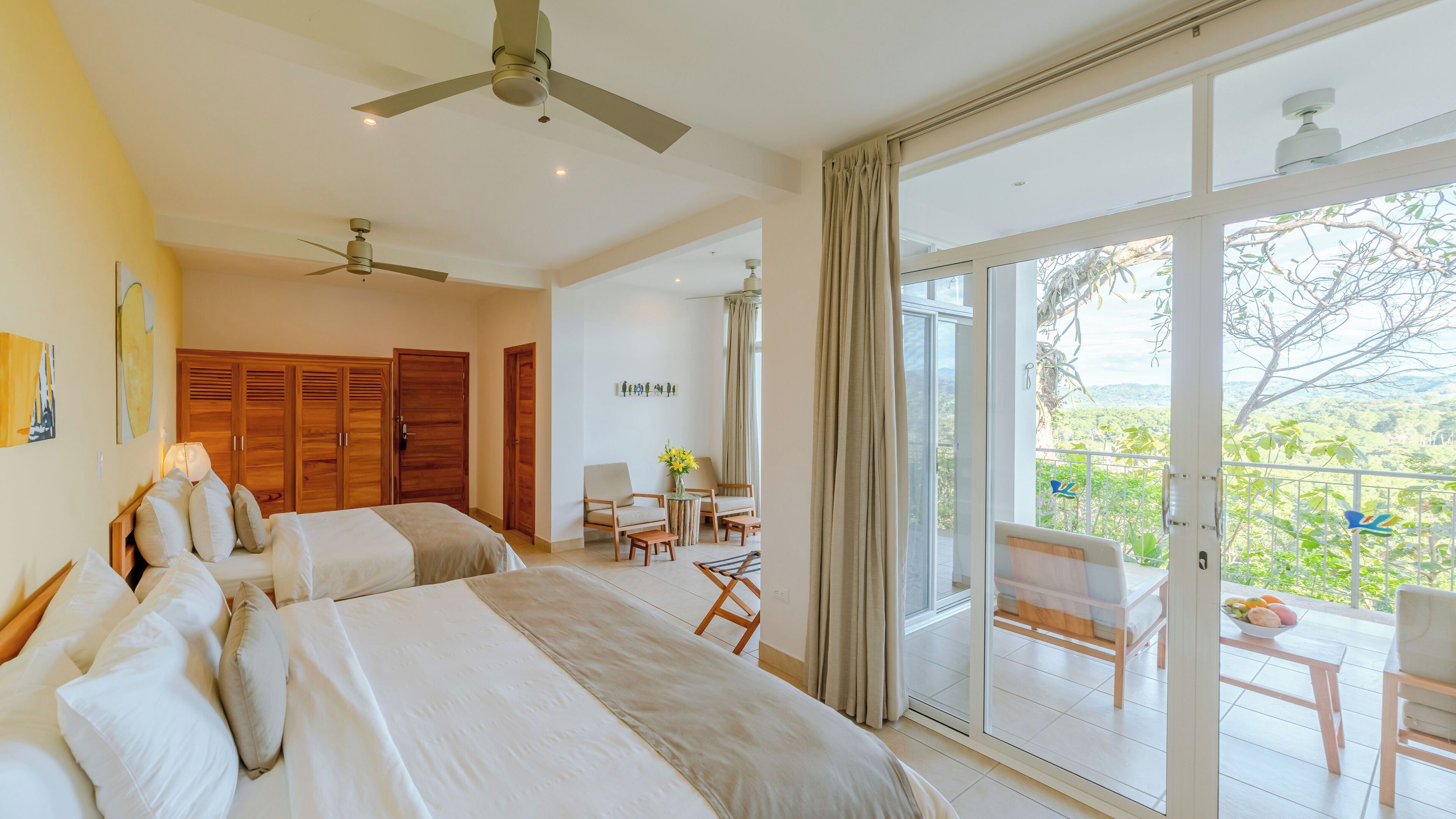 A hotel room with two beds, a balcony with a table and chairs, and a view of the outdoors.