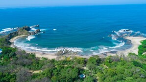 Vista aérea de una zona costera con playa, afloramientos rocosos y abundante vegetación.