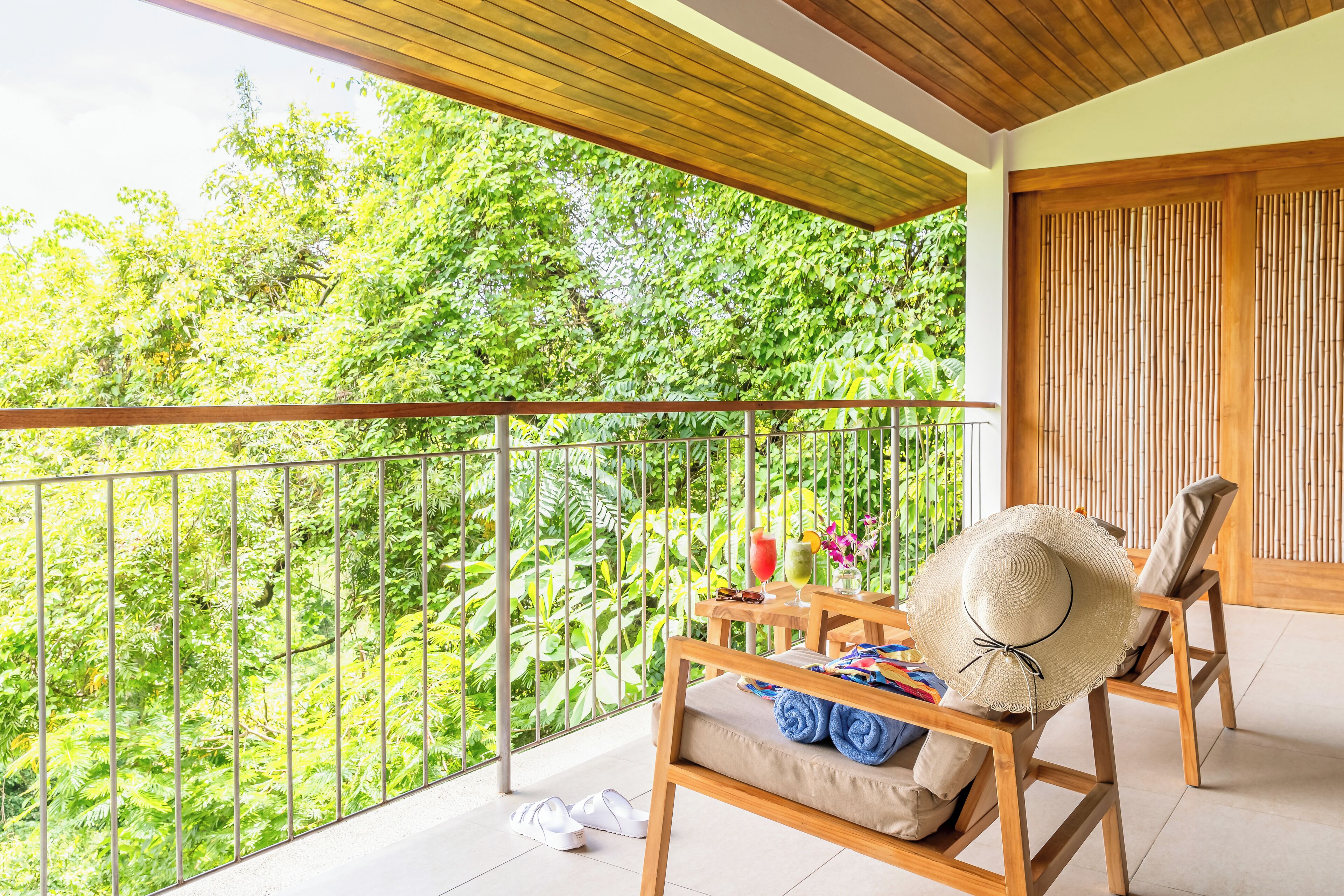 A balcony with a wooden chair, a table with a hat, and a pair of slippers.