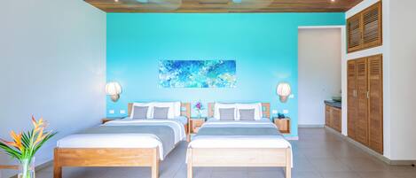 A modern hotel room with two wooden beds, a blue accent wall, and a ceiling fan.