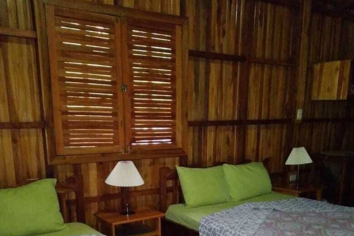 A room with two beds, wooden walls, and a window with blinds.
