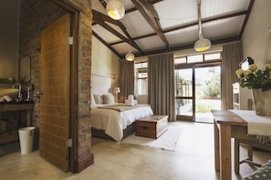 A bedroom with a bed, bedside tables, a wooden bench, a window with curtains, and a view of the outdoors.
