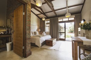 Un dormitorio con cama, mesitas de noche, un banco de madera, una ventana con cortinas y vistas al exterior.