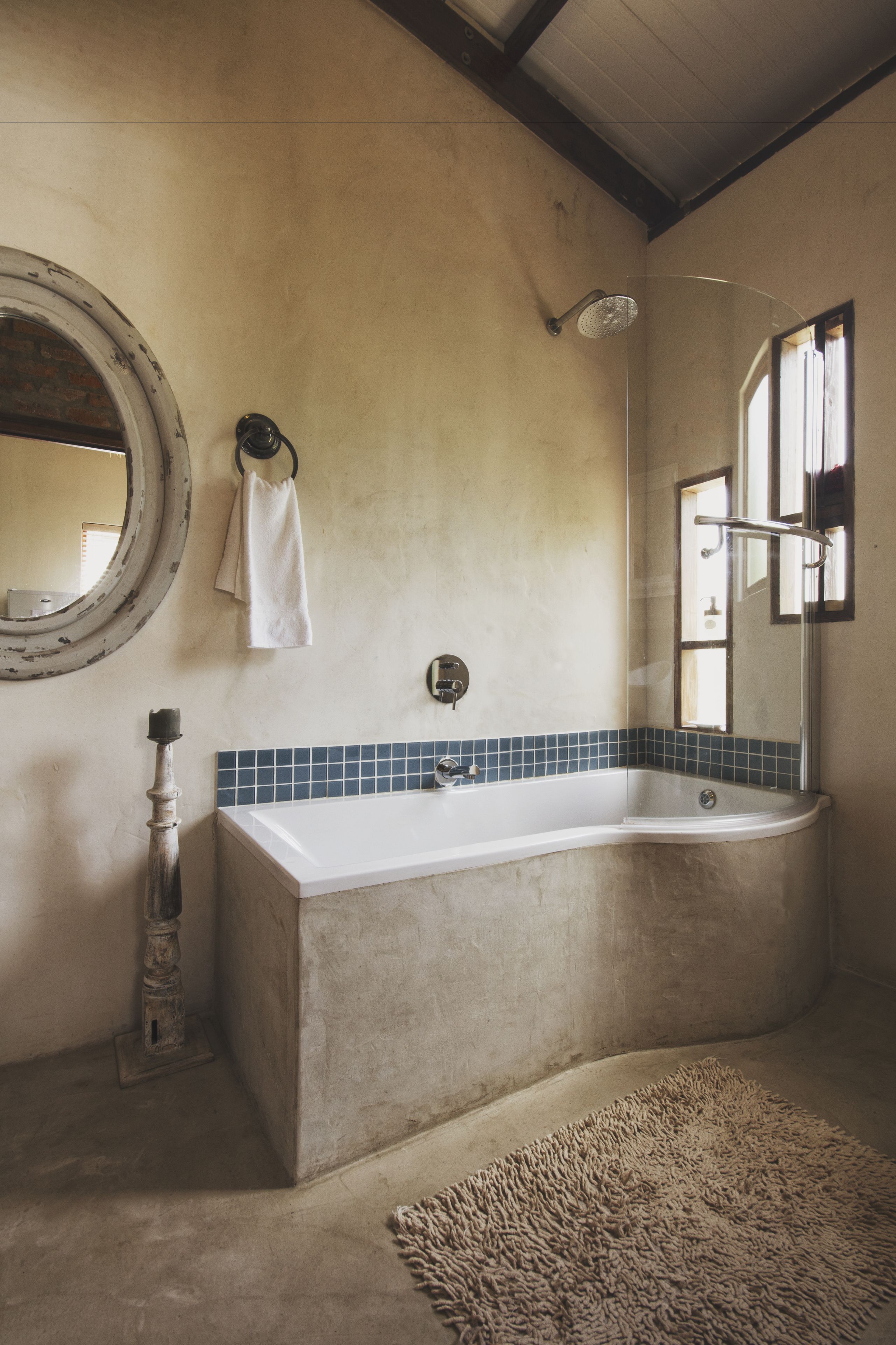 A bathroom with a large bathtub, a round mirror, and a shower area.
