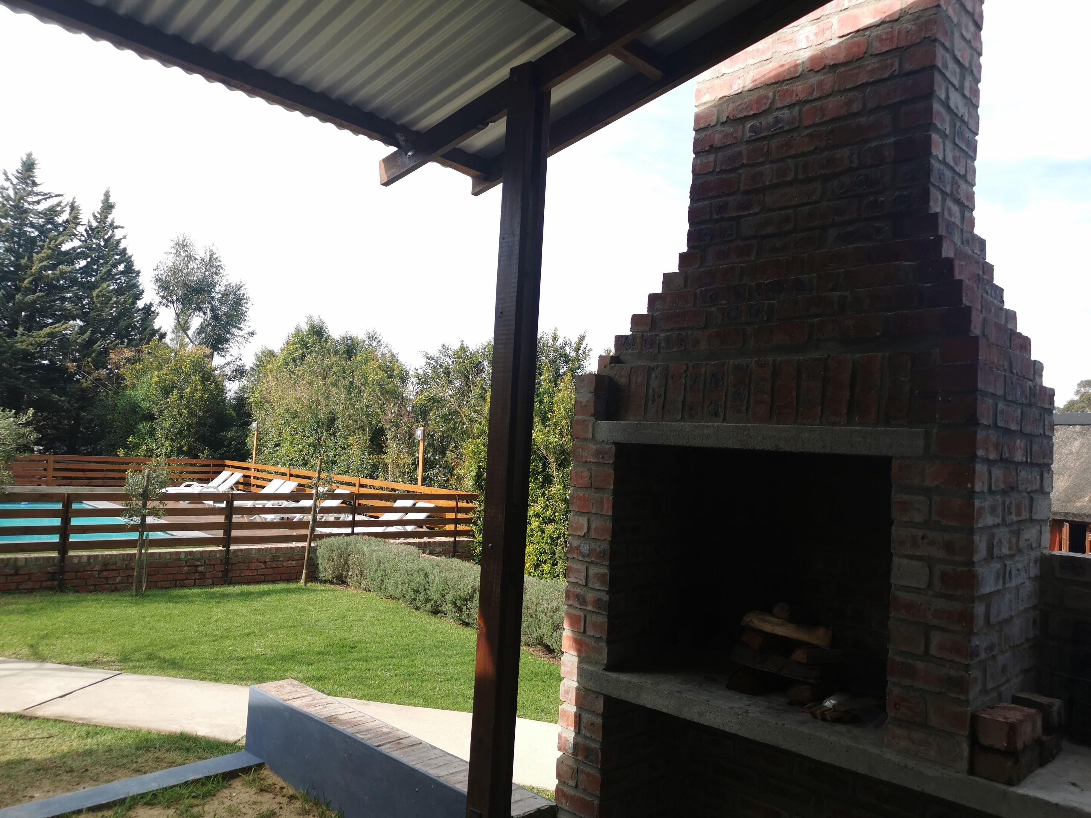 Cucina esterna in mattoni con un camino, circondata da un pontile in legno e una piscina.