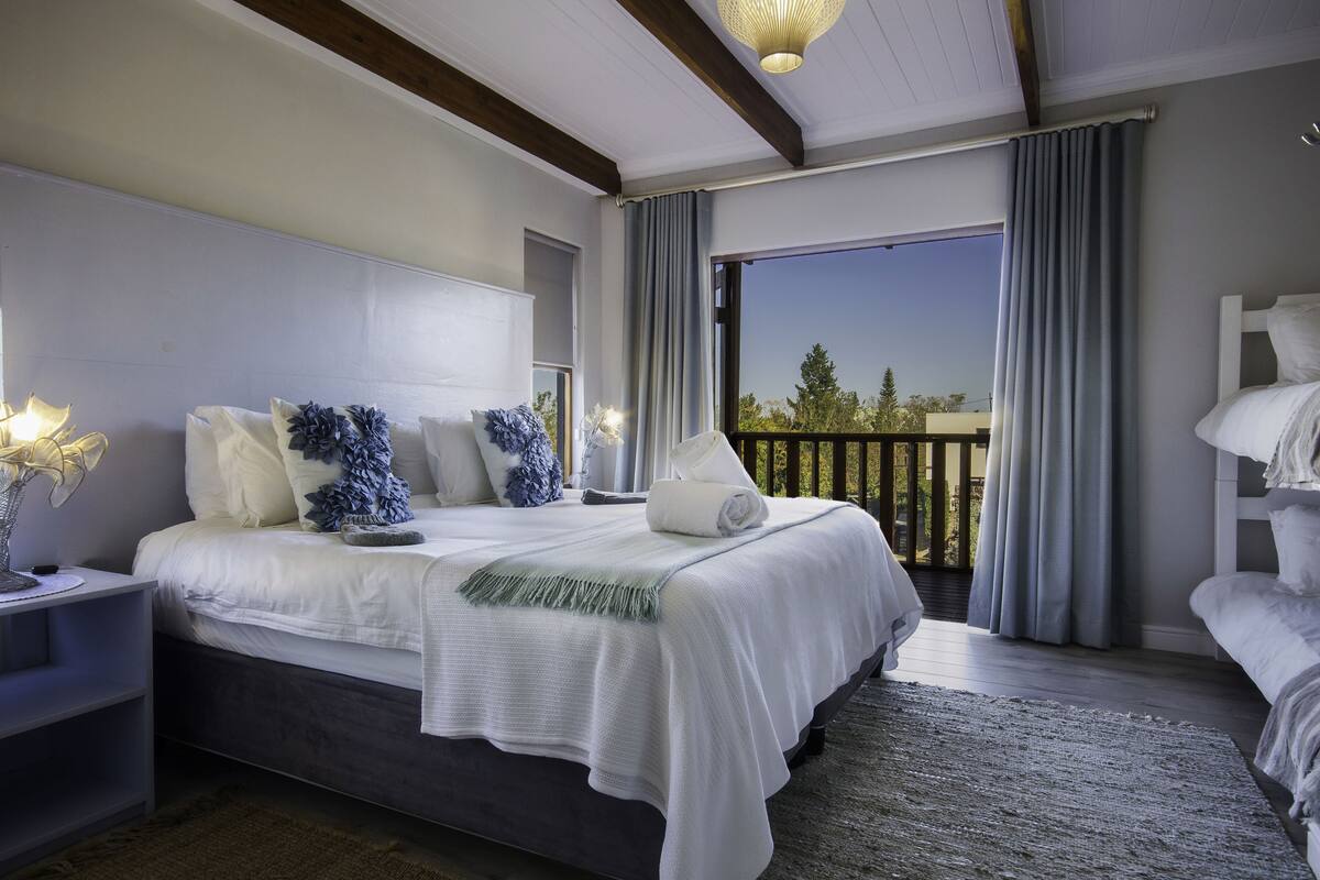 Een slaapkamer met een groot bed, een nachtkastje, een dressoir en uitzicht op de omgeving vanaf een balkon.
