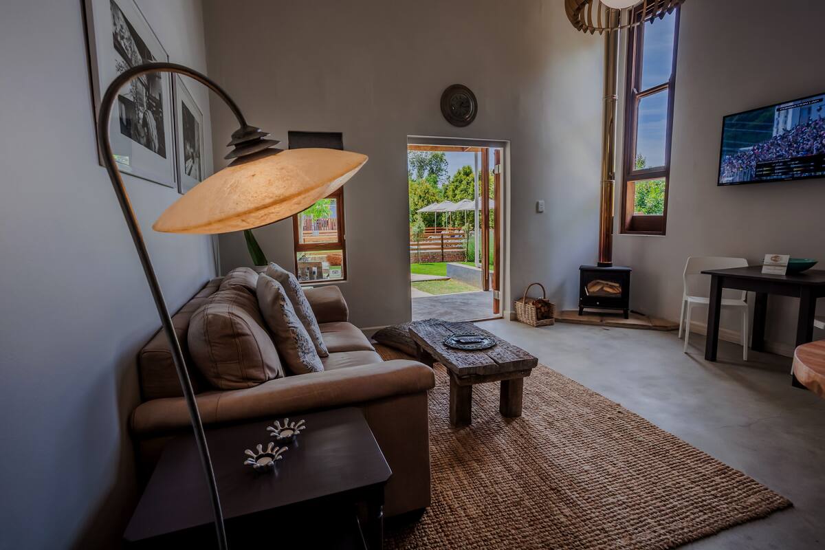 Een moderne woonkamer met een bank, een salontafel, een lamp en een televisie. Er is een deur naar een buitenruimte met een terras en een open haard.