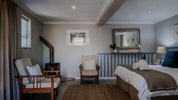 Un dormitorio con cama, dos sillas, chimenea, espejo y obras de arte en la pared.