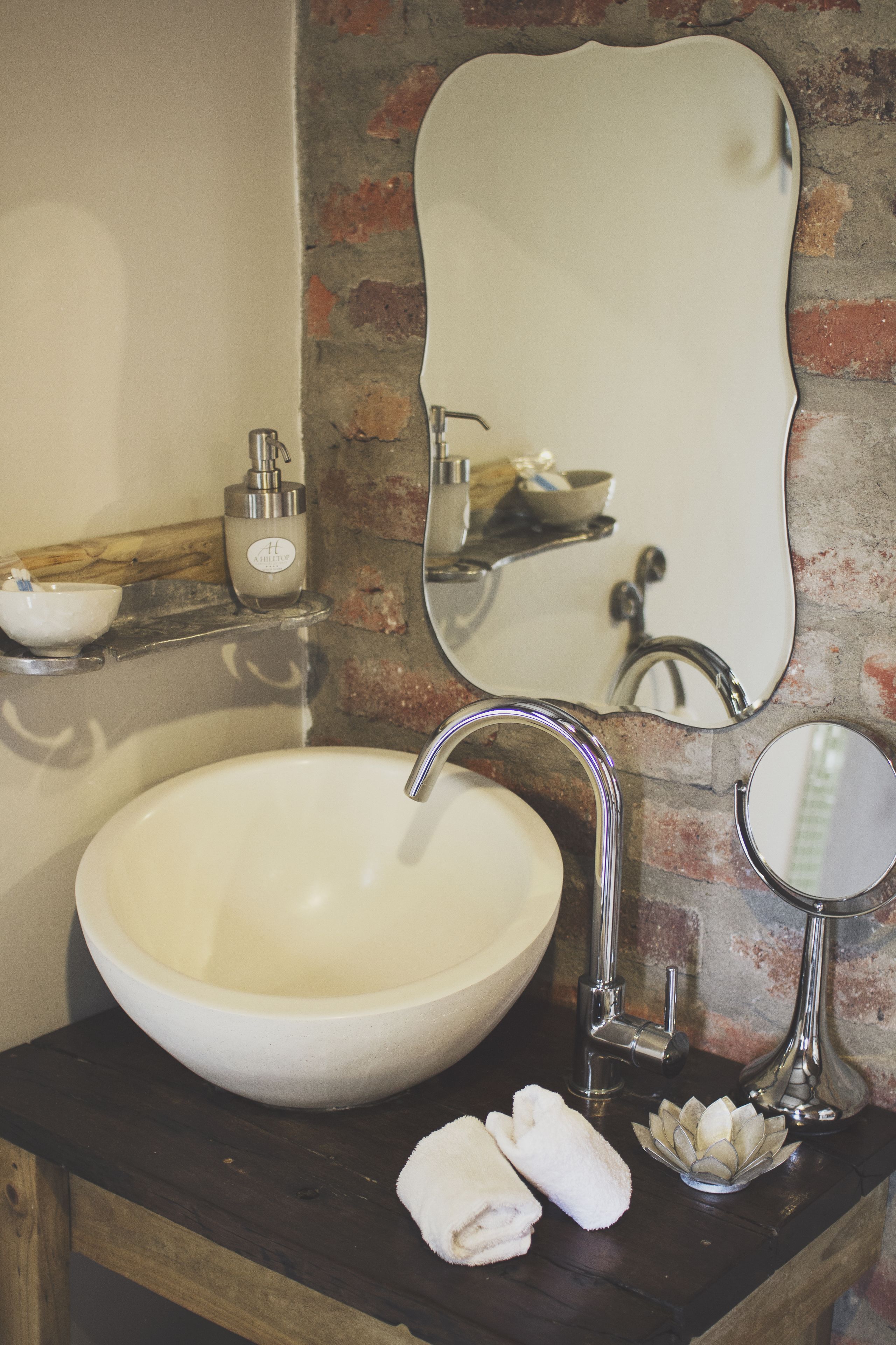 A bathroom with a large white sink, a mirror, and a soap dispenser on a wooden countertop.