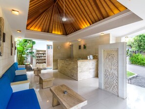 A modern lobby with a wooden ceiling, a reception desk, and a seating area with blue sofas. - Artemis Villa (Seminyak)