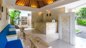 A modern lobby with a wooden ceiling, a reception desk, and a seating area with blue sofas. - Artemis Villa (Seminyak)