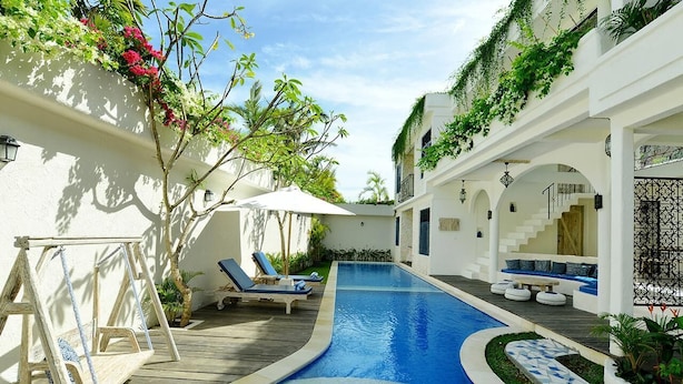 A pool area with a wooden deck, lounge chairs, and a staircase leading to an upper level. - Artemis Villa (Seminyak)