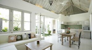 A bright, open-plan living area with a kitchen, large windows, and a ceiling with exposed beams. - Artemis Villa (Seminyak)