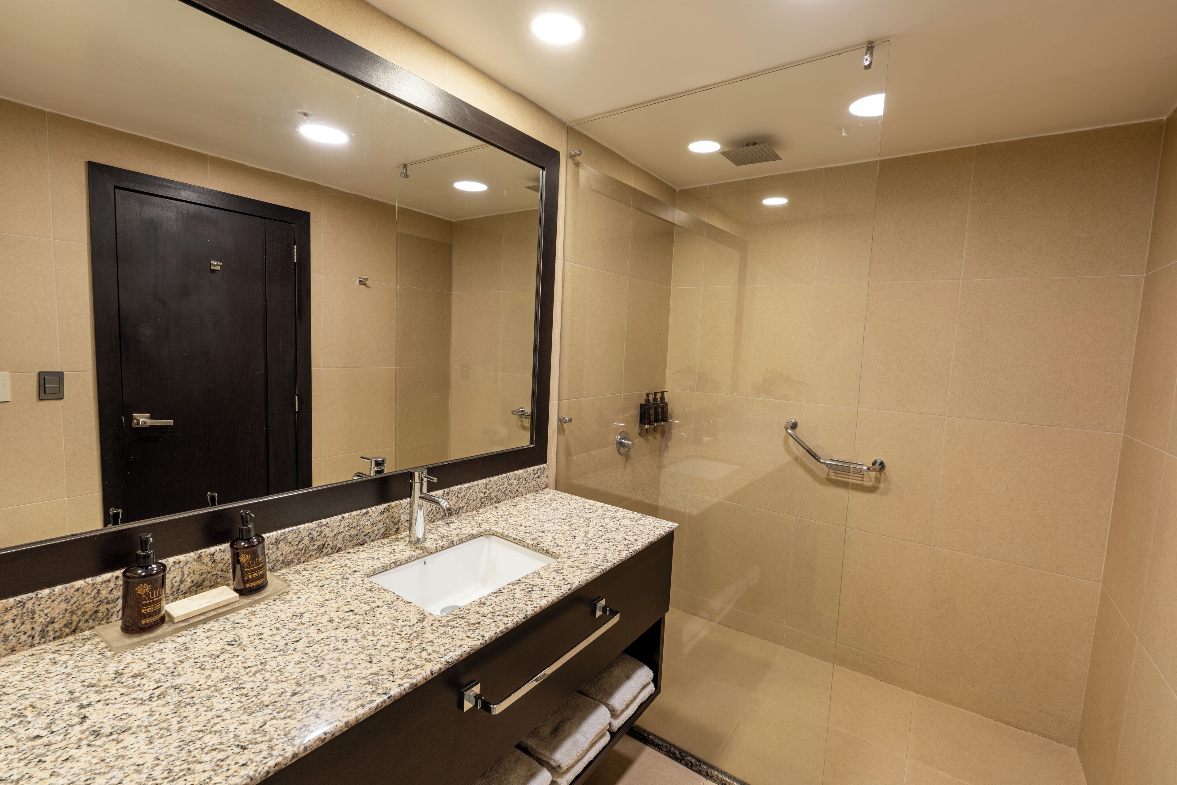 Un baño moderno con encimera de granito, lavamanos, espejo y zona de ducha.