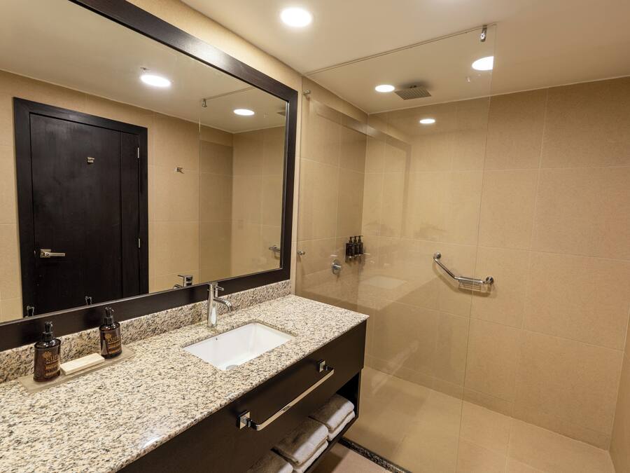Un baño moderno con encimera de granito, lavamanos, espejo y zona de ducha.