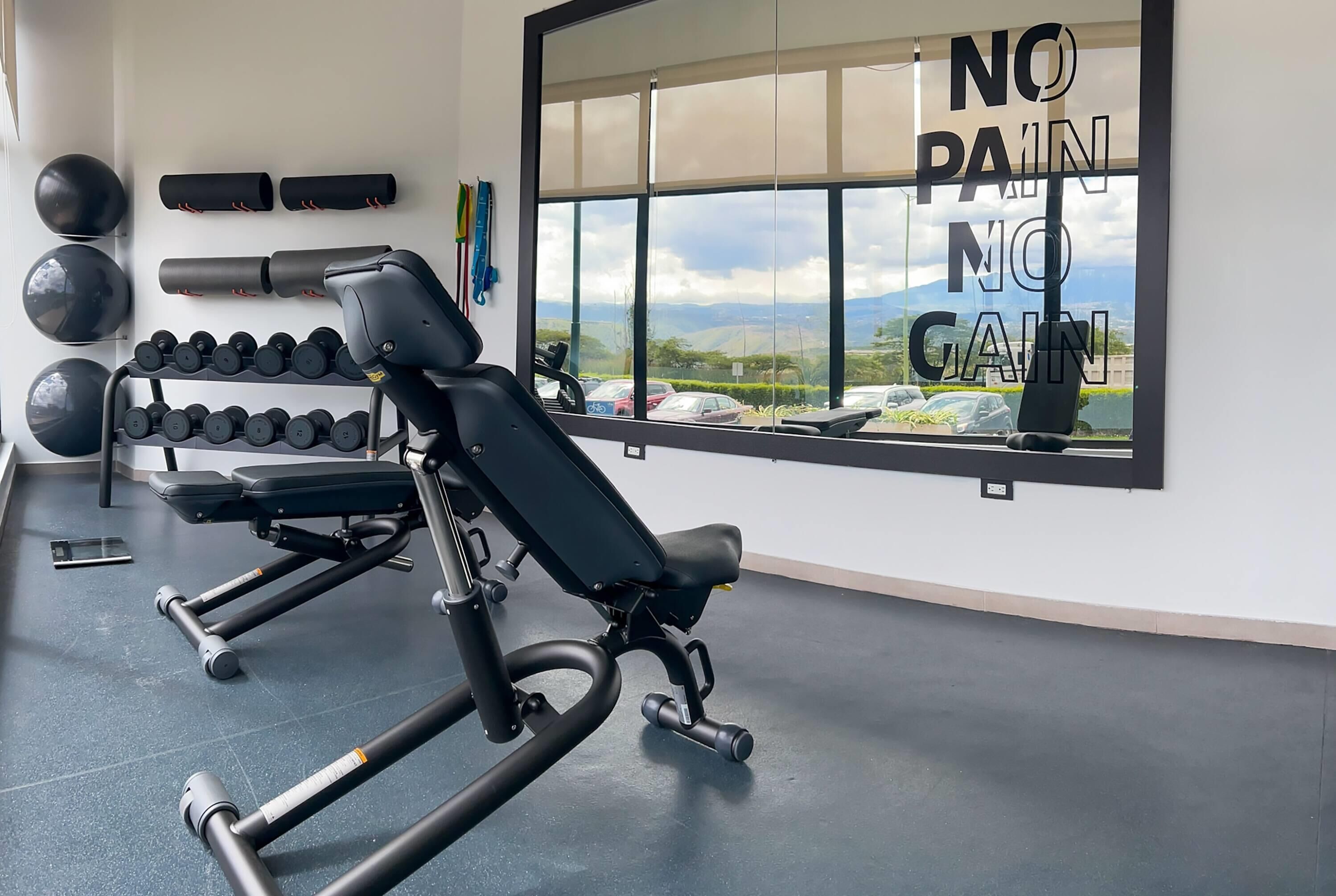 Un gimnasio con equipo de ejercicio, una banca y una frase motivacional en la pared.