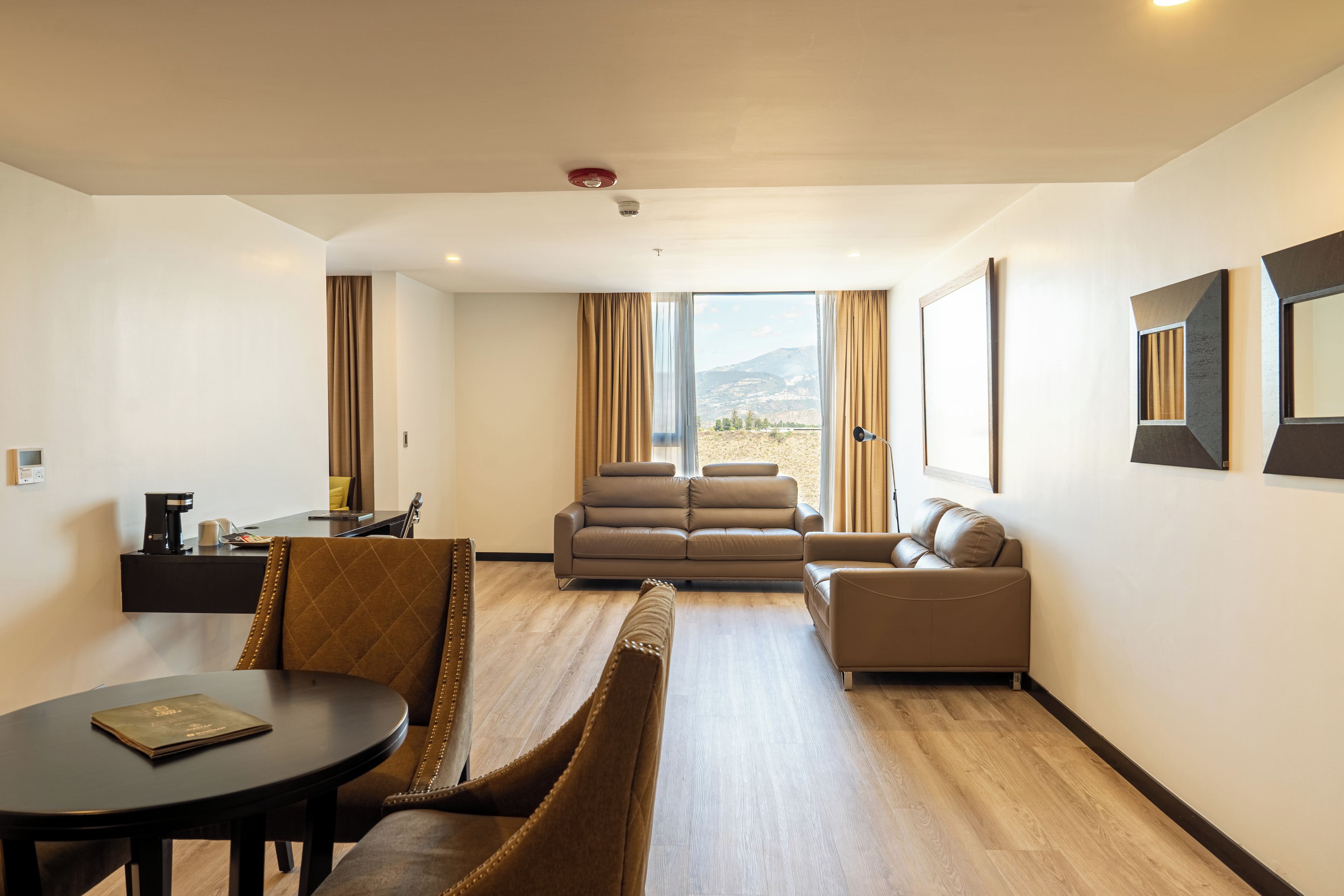A modern hotel room with a dining area, a sofa, and a view of the outdoors.