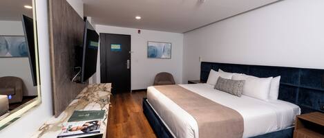 A modern hotel room with a large bed, a flat-screen TV, a wooden floor, and a marble-patterned bench.