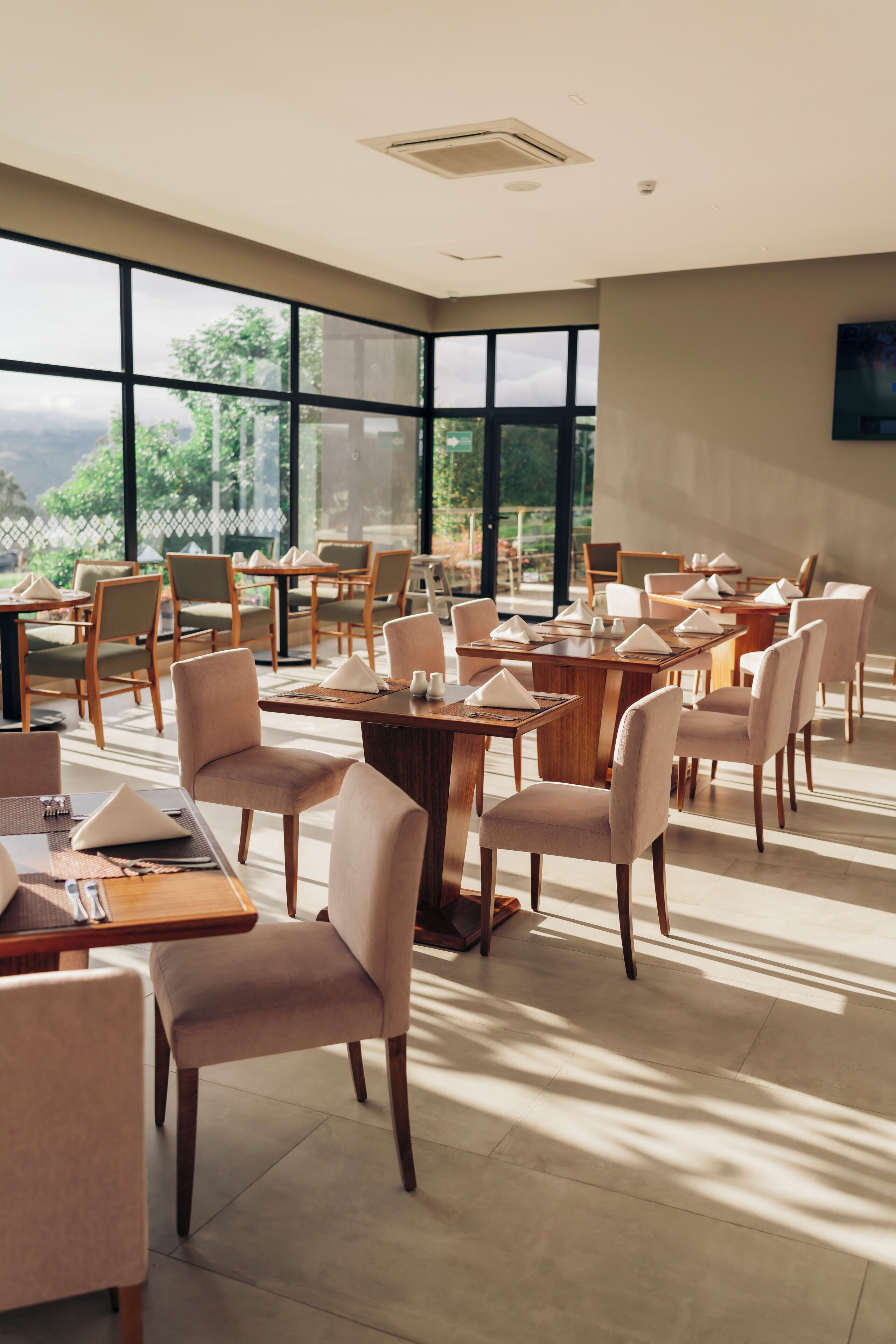Un vaste espace dédié à la salle à manger, avec de nombreuses tables et chaises, et de grandes fenêtres donnant sur un paysage verdoyant.