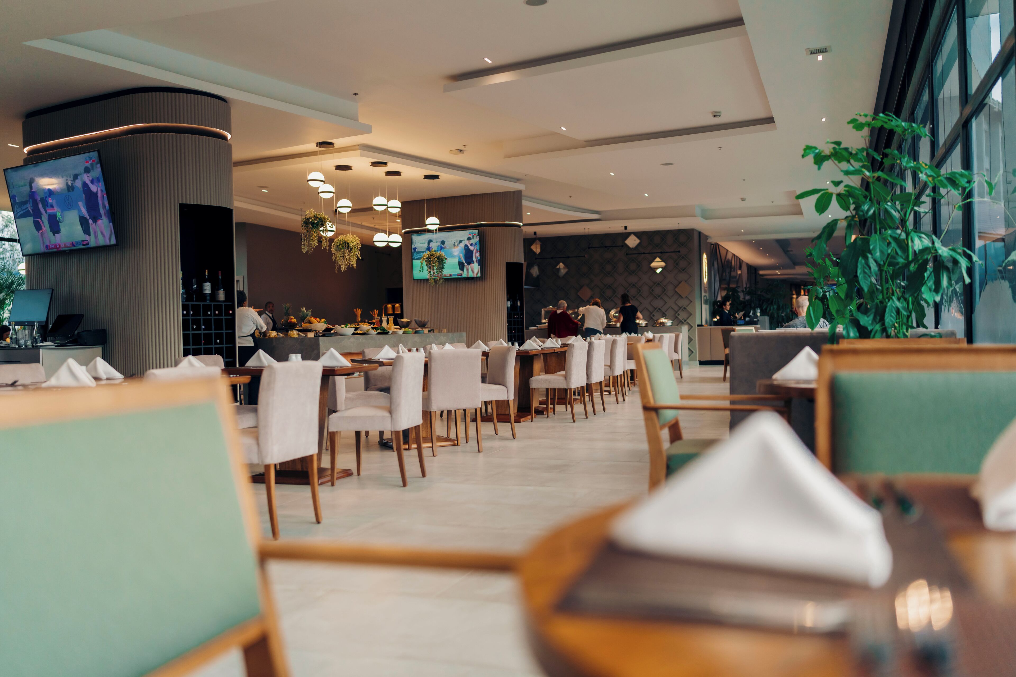 Un restaurant moderne doté de plusieurs tables et chaises, d’un bar et d’un écran de télévision fixé au mur.