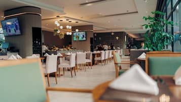 Un restaurant moderne doté de plusieurs tables et chaises, d’un bar et d’un écran de télévision fixé au mur.