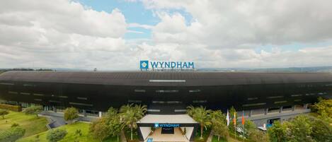 A large, modern building with a prominent 'WYNDHAM' sign, surrounded by greenery and palm trees.