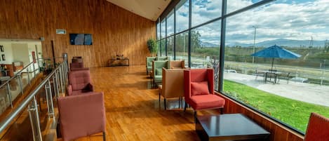 Un vestíbulo amplio con suelo de madera, ventanas grandes que ofrecen vistas al exterior y zonas de estar con mobiliario moderno.