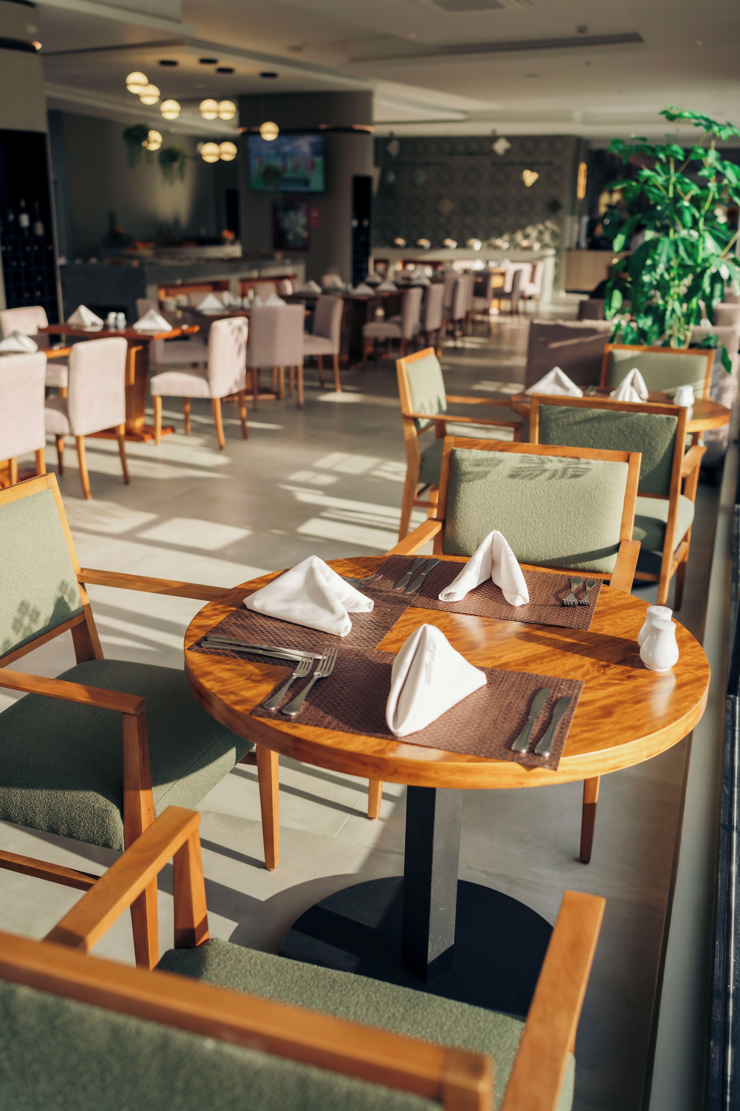 A restaurant with round tables, green cushioned chairs, and a bar area in the background.