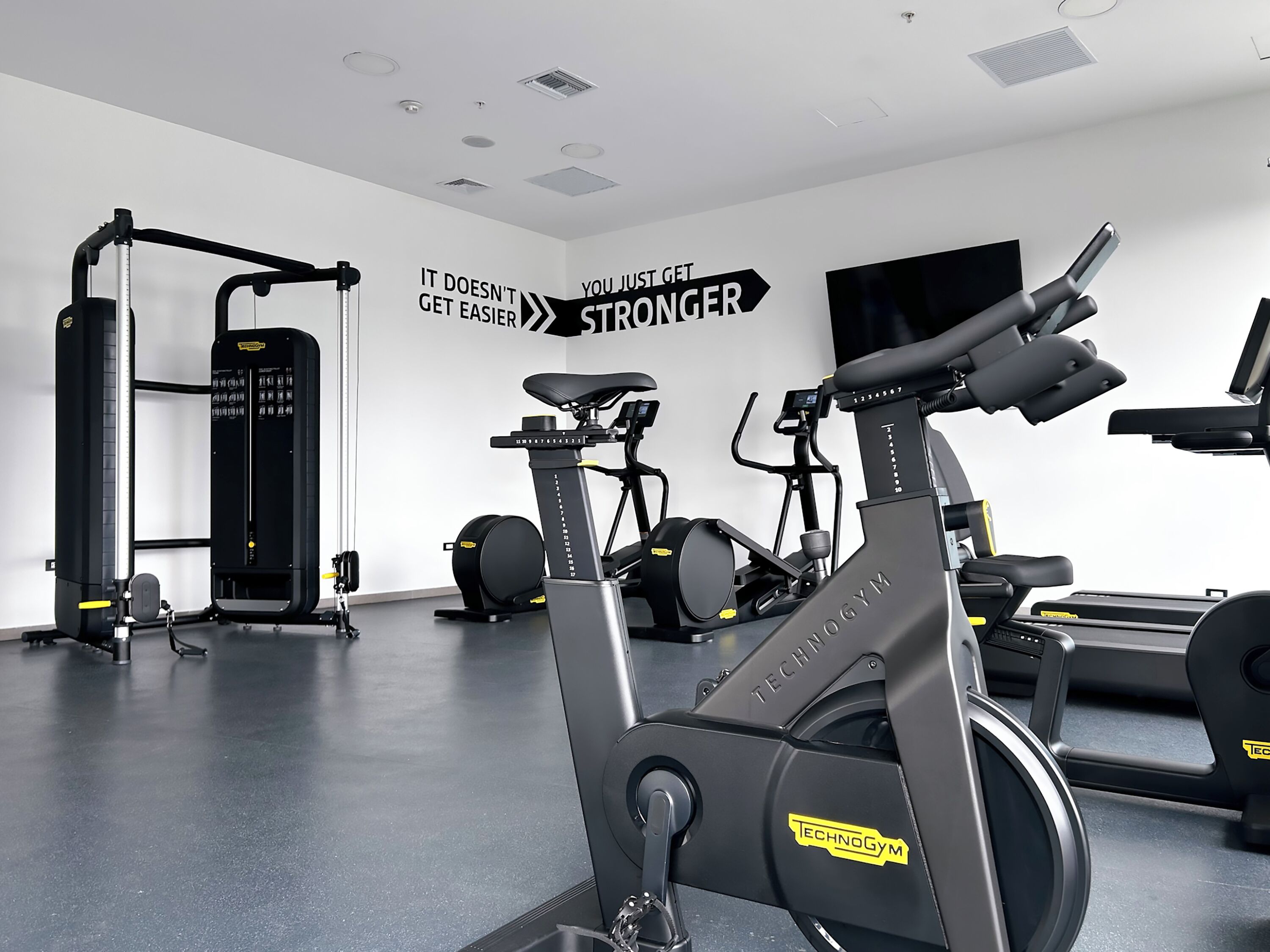 A gym with exercise equipment, a motivational wall, and a large TV screen.