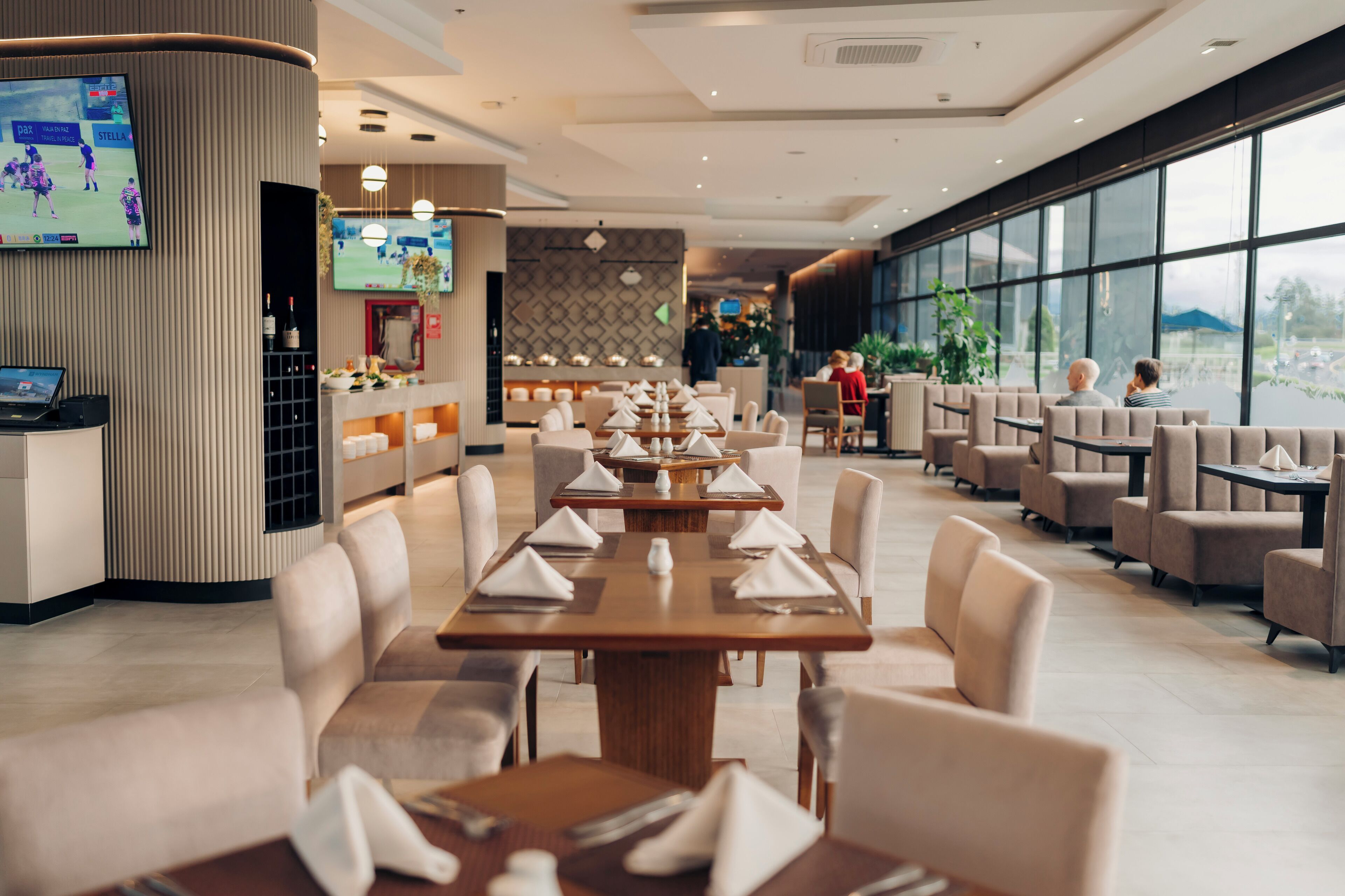 Un restaurante moderno con mesas largas dispuestas para comer, una zona de bar y amplias ventanas que ofrecen vistas.