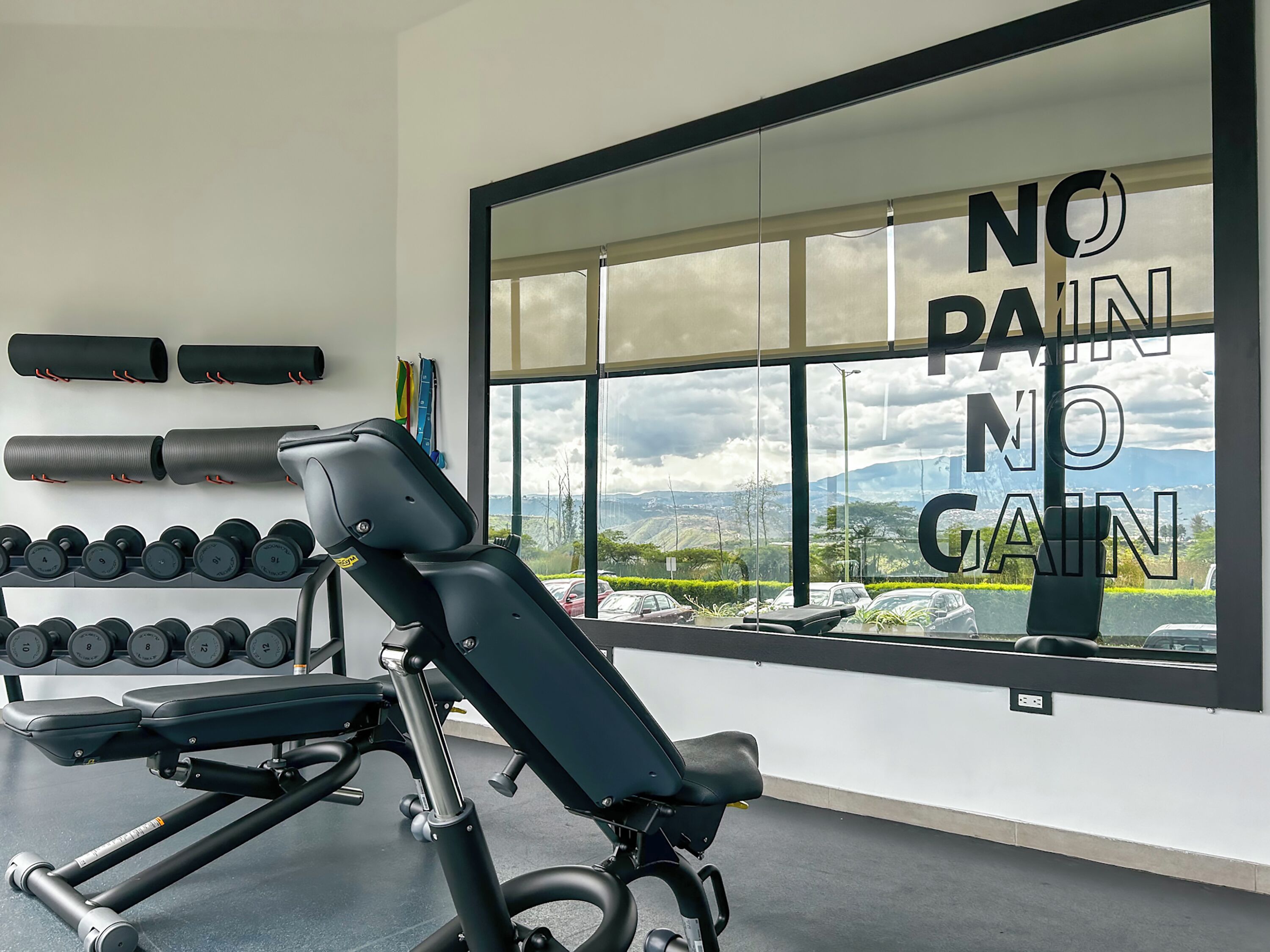 A gym with a bench press, dumbbells, and a motivational quote on the window.