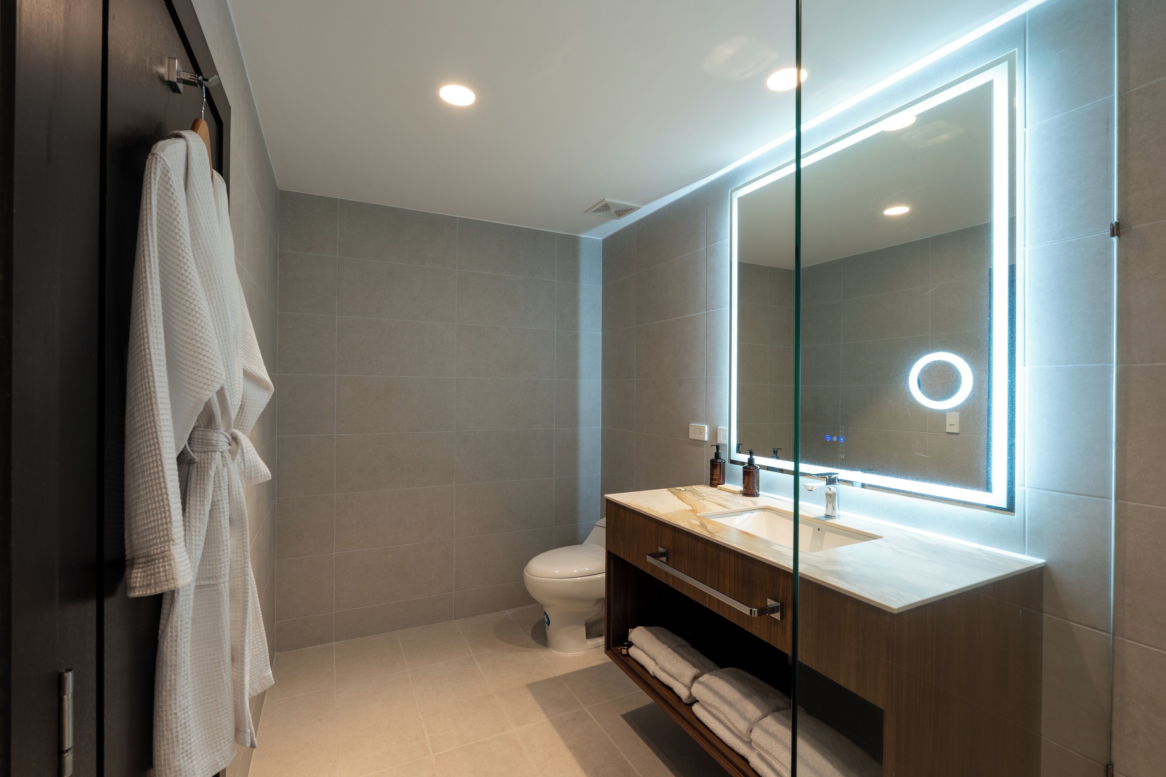 A modern bathroom with a large mirror, a toilet, and a vanity with a towel rack.